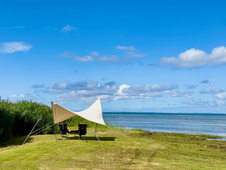 Lavvandet kyst ved Dråby Strand med solsejl og udsigt over Isefjorden en sommerdag